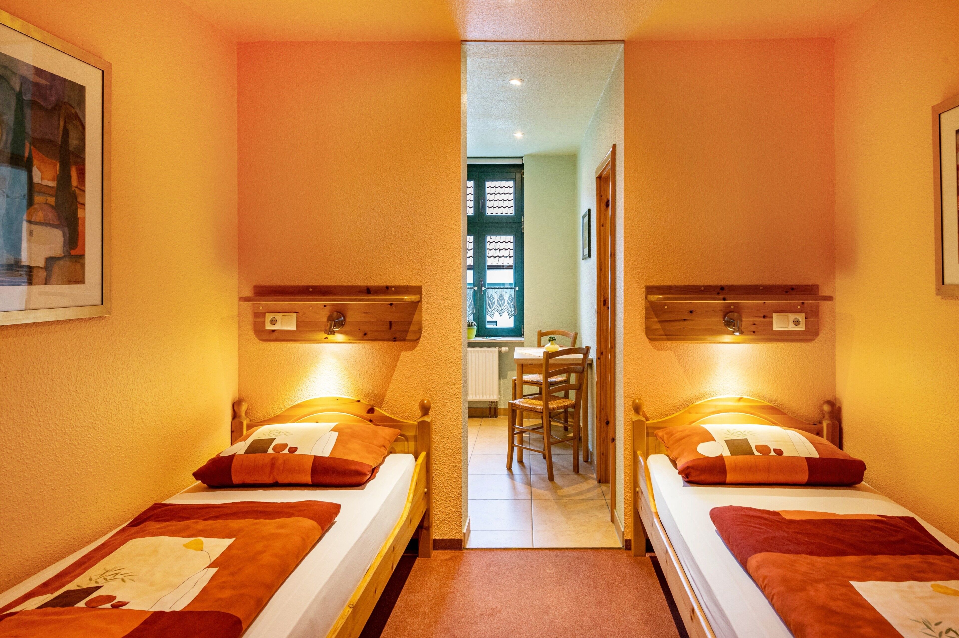 Ein Zimmer mit zwei Einzelbetten, einem Holz-Kopfteil, einem kleinen Tisch und einem Stuhl.
