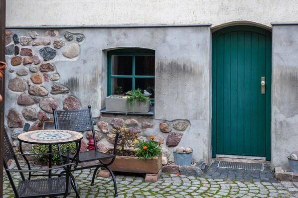 A stone building with a green door, a window with plants, and a table with chairs.