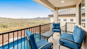 Un balcon avec des chaises bleues et une petite table, donnant sur une piscine et un paysage désertique.