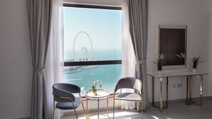 Una habitación con un ventanal grande, dos sillas, una mesita redonda y un cuadro en un atril.