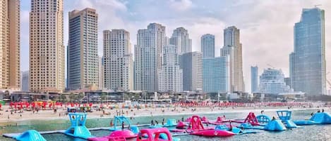 A beach with water taxis and tall buildings in the background.