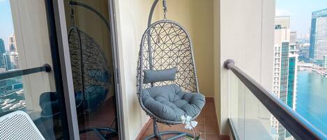 Un balcón con una silla de metal blanco, una silla colgante y una mesita con tazas y una planta.