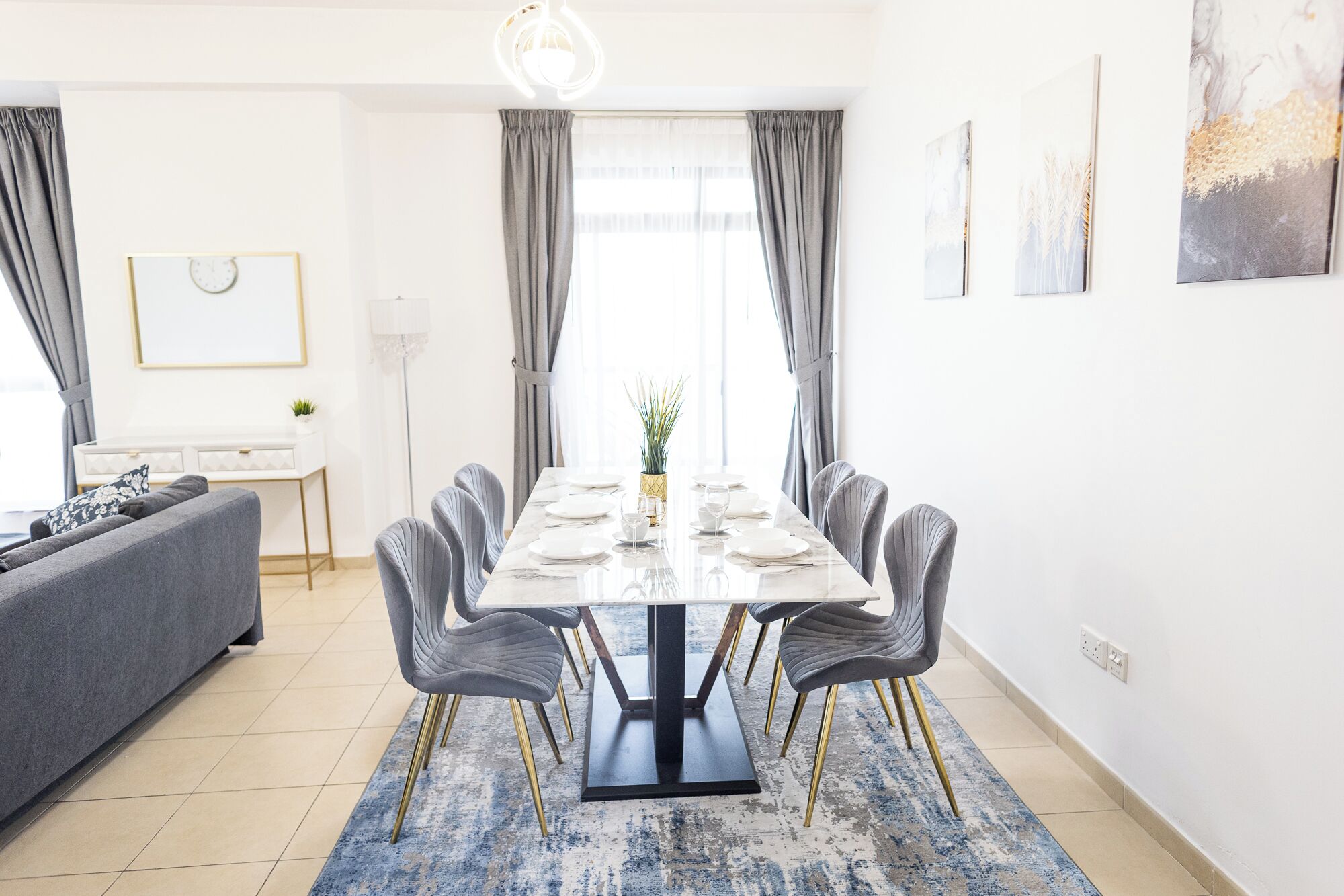 Een moderne eetruimte met een marmeren tafel, gestoffeerde grijze stoelen en een blauw tapijt met patroon.
