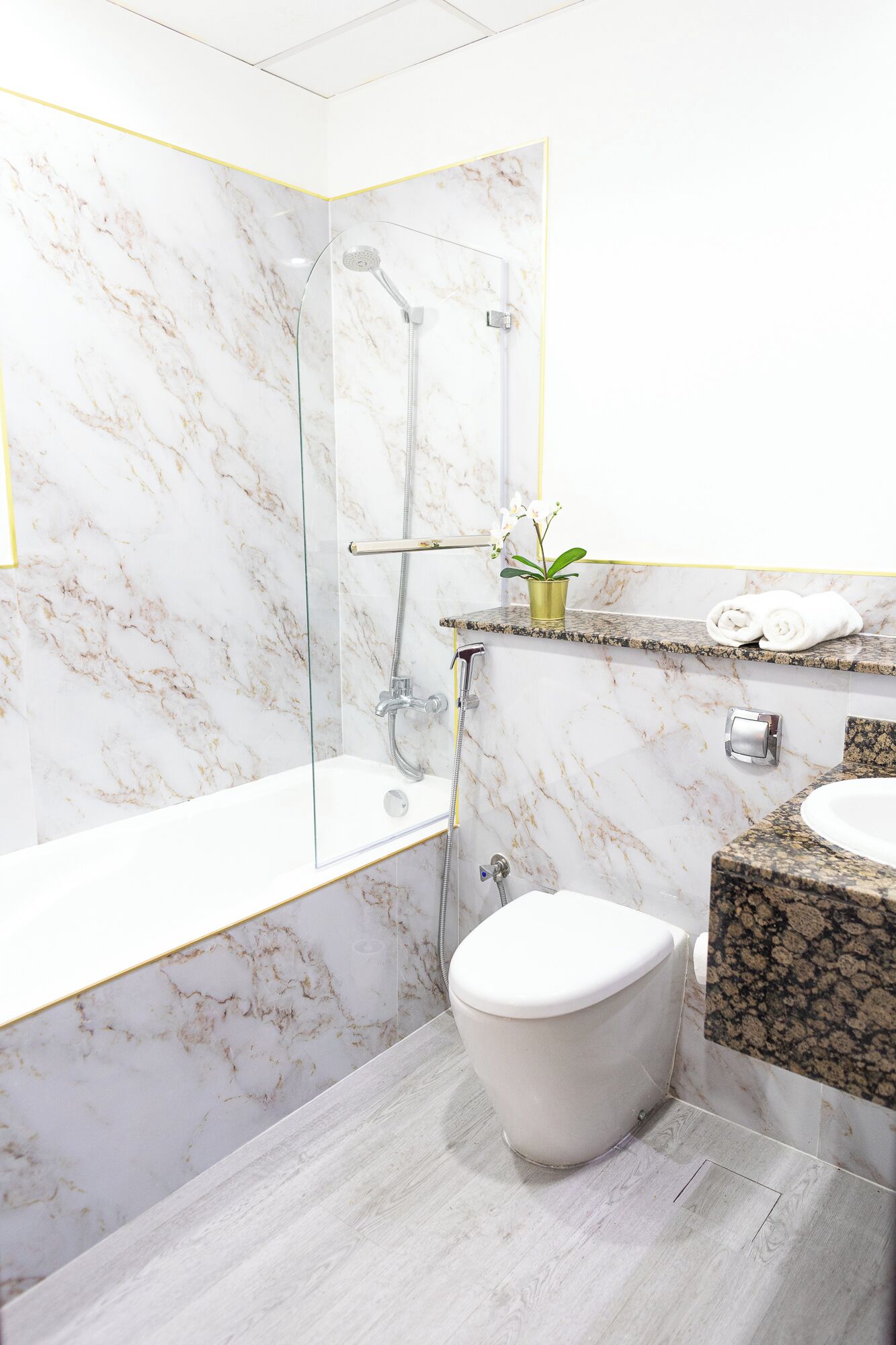 A modern bathroom with a marble shower enclosure, a toilet, and a granite countertop sink.