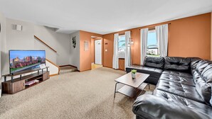 Ein modernes Wohnzimmer mit einem Flachbildfernseher, einem Ledersofa, einem kleinen Tisch und einer Treppe.