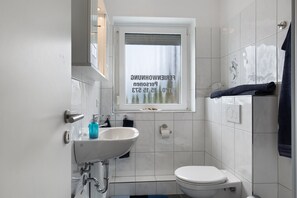 Ein Badezimmer mit weißem Waschbecken, Toilette und einem Fenster mit Blick auf Bäume.