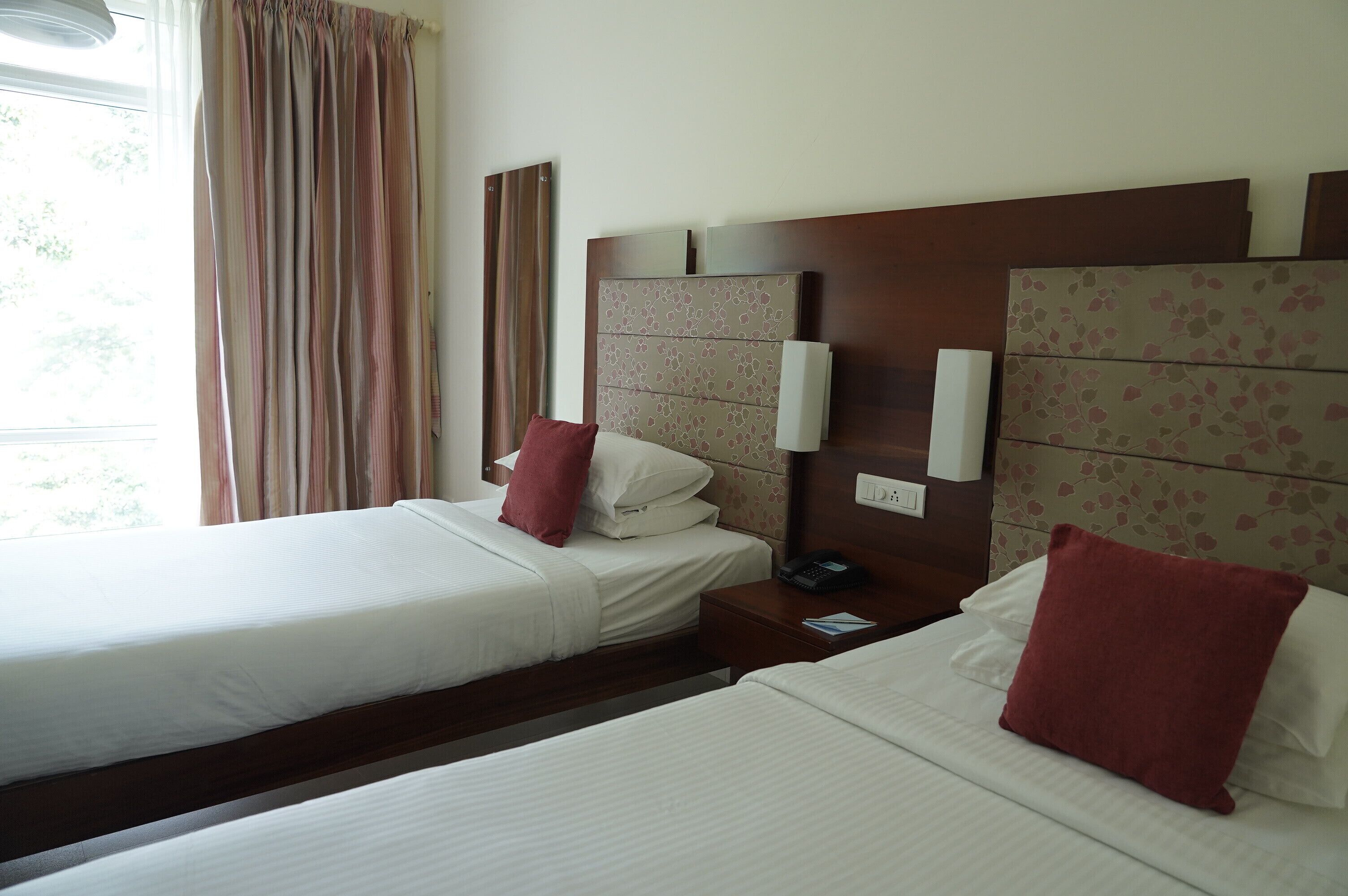 A hotel room with two single beds, each with a pillow and a bedside table with a phone.