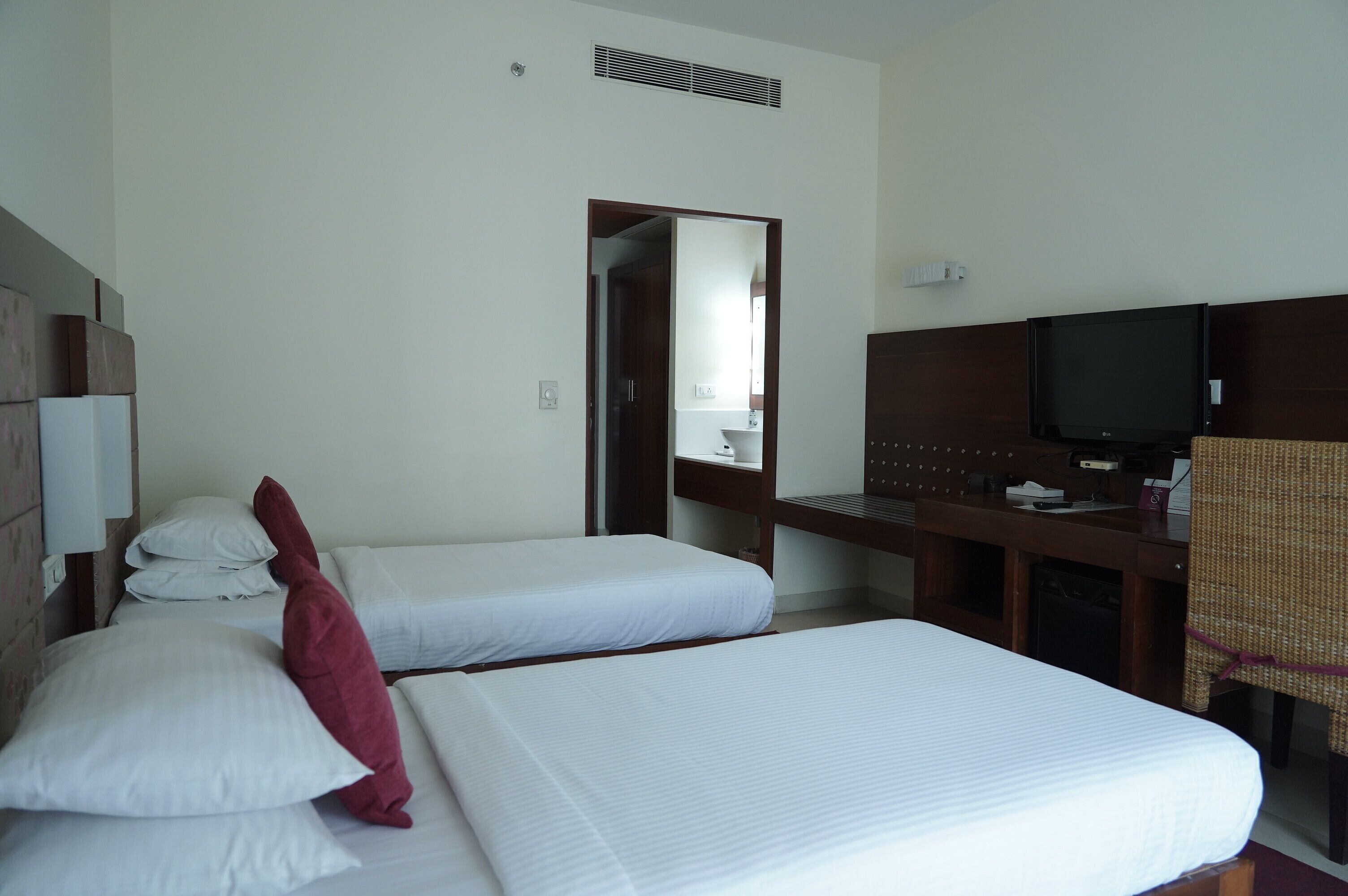 A hotel room with two single beds, a television, a desk, and a mirror.