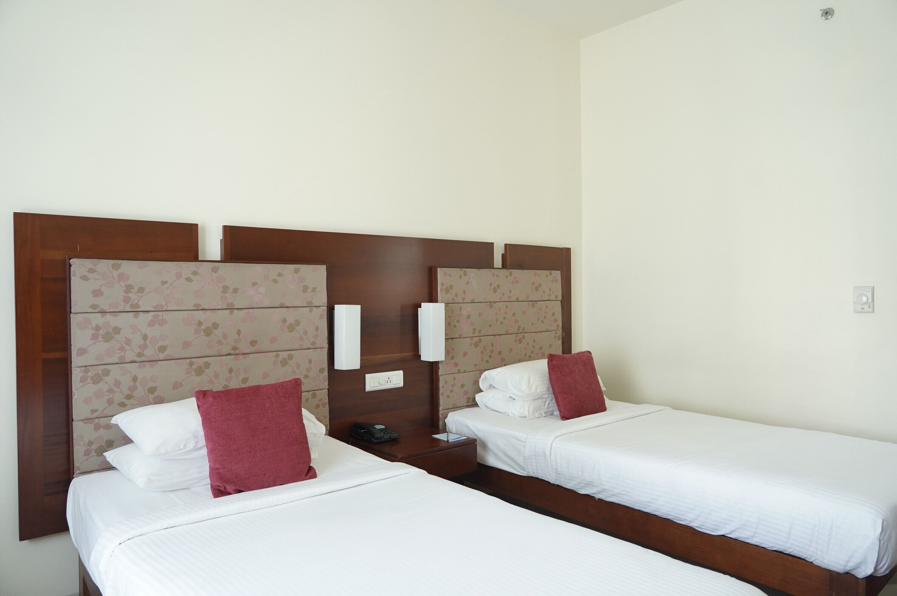 A hotel room with two single beds, wooden headboards, white bedding, and a nightstand with a phone and a book.