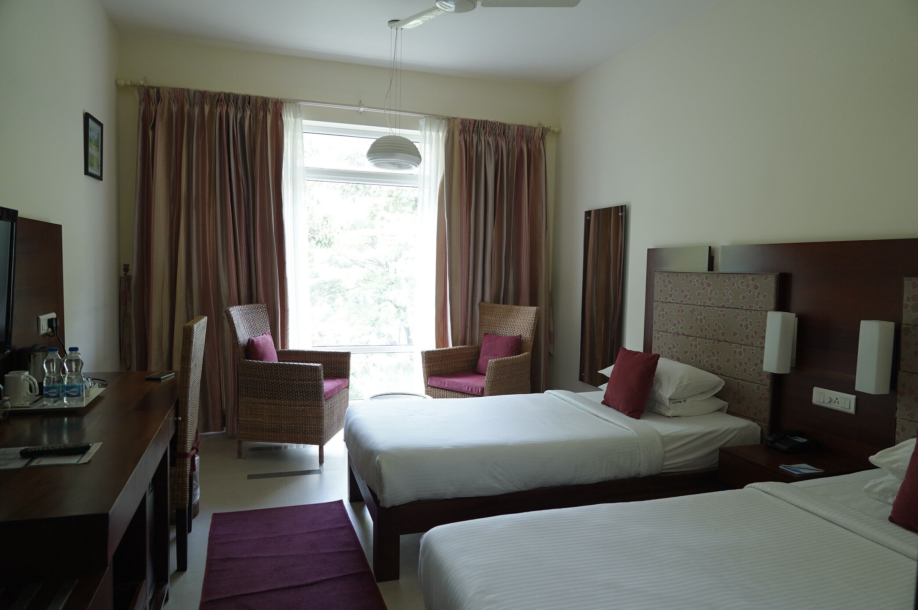 A hotel room with two beds, a desk, a chair, and a window with curtains.