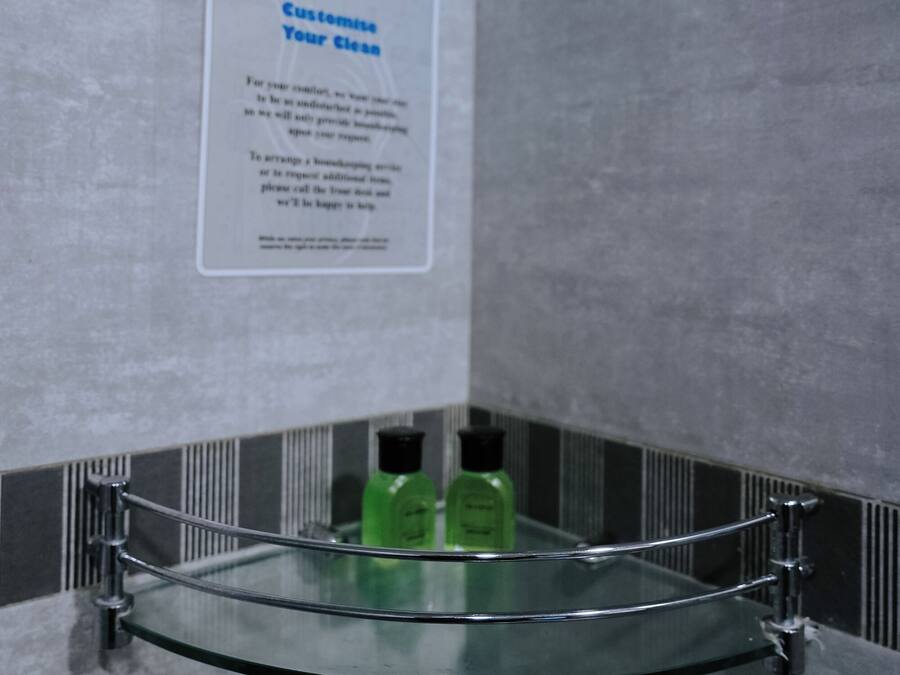 A bathroom with a glass shelf holding toiletries, a sign on the wall, and a showerhead.