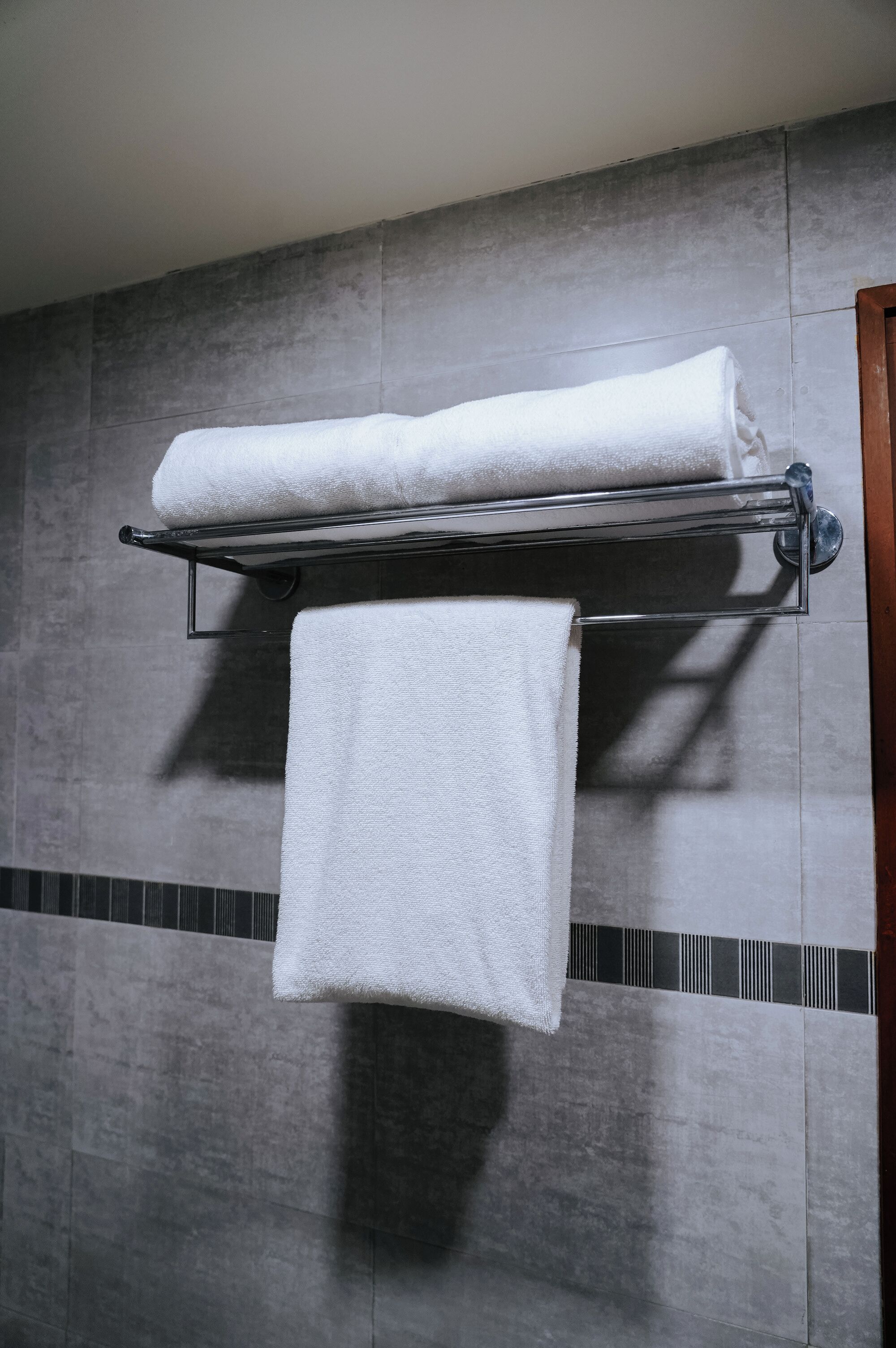 Un baño con baldosas grises, un perchero con dos toallas y una puerta de madera.