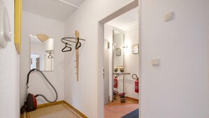 Ein Flur mit Staubsauger, Spiegel, Feuerl öscher und einer Tür zum Badezimmer.