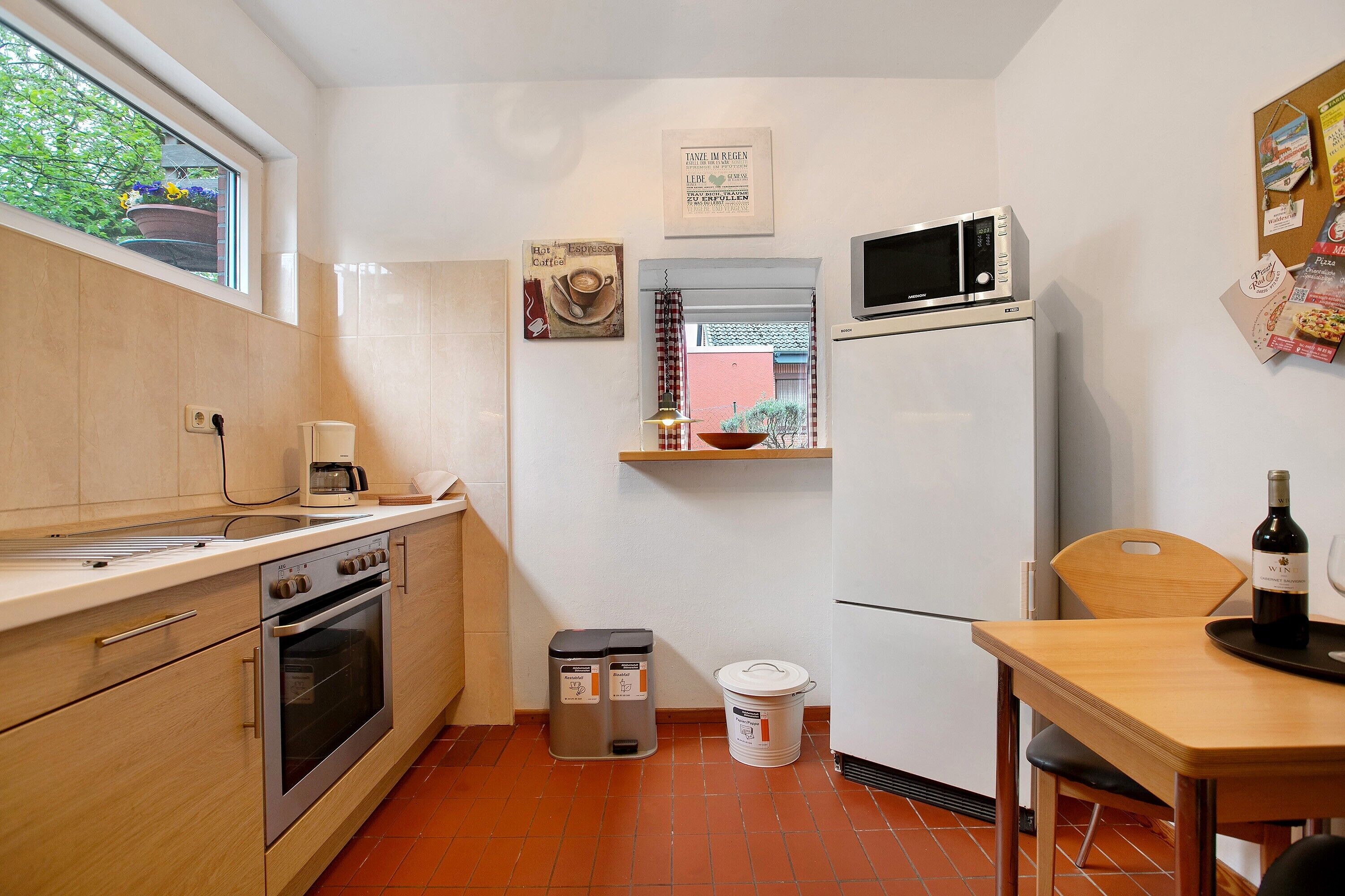 A compact kitchen with a microwave, oven, and sink. There is a wooden table with a bottle of wine and a tray.