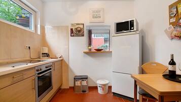 A compact kitchen with a microwave, oven, and sink. There is a wooden table with a bottle of wine and a tray.