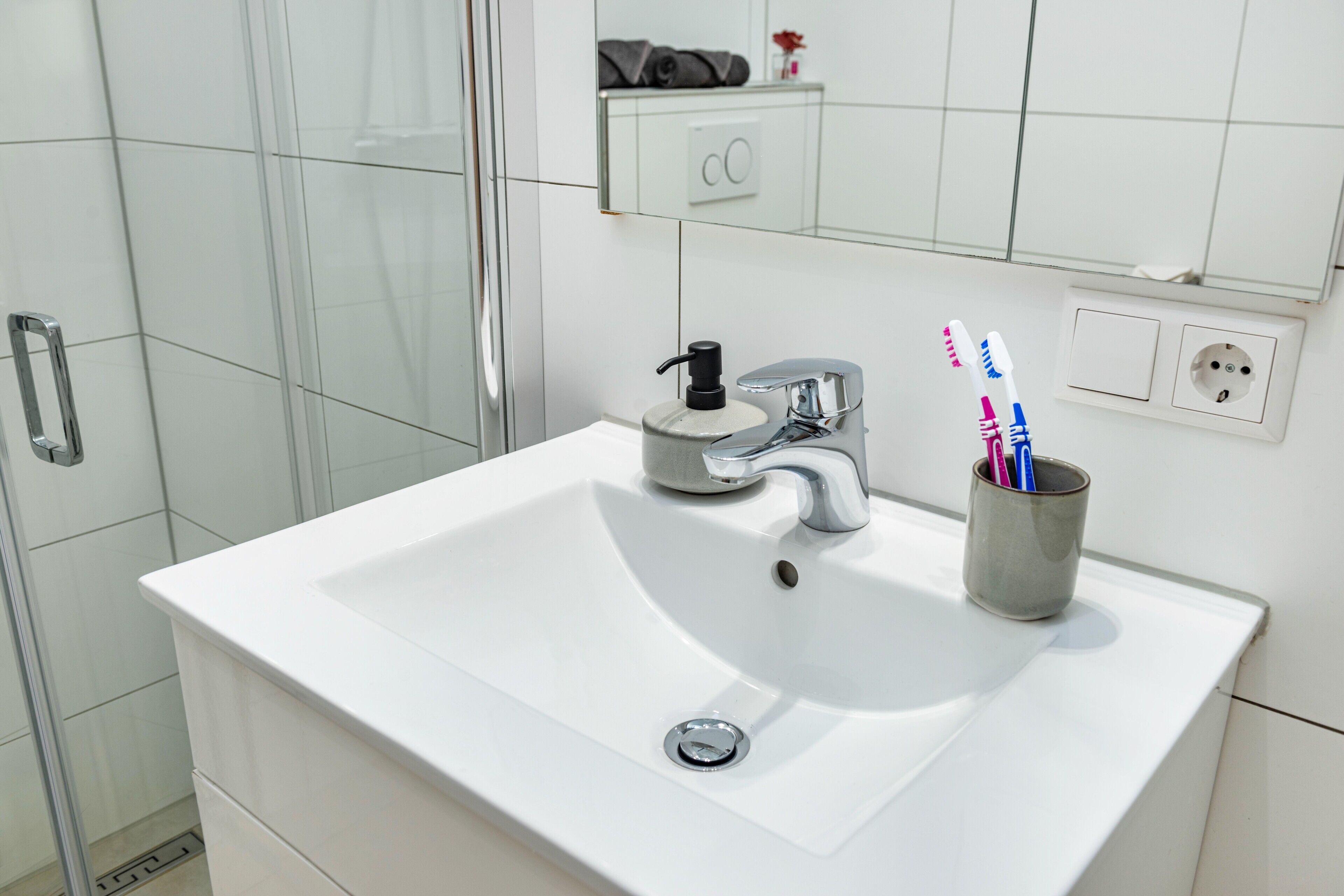 A bathroom with a white sink, chrome faucet, and a cup holding toothbrushes.
