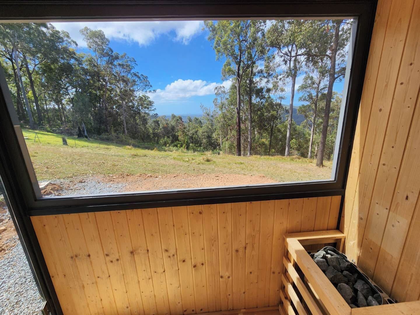 Ein Holzinnenraum mit einem großen Fenster mit Blick auf eine Wiese und Bäume.