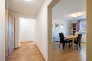 A room with a wooden floor, a dining table with chairs, a radiator, and a window with curtains.