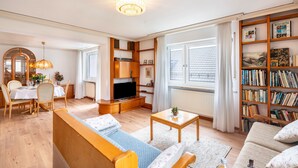 Una sala de estar con un sofá, televisor, mesa de comedor con sillas y una estantería.