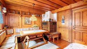 Interior de una cabaña de madera con una mesa de comedor, bancos, una araña y un aparador con cristalería.