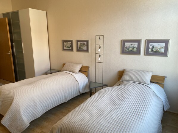 Habitación de hotel con dos camas individuales, una mesita de noche, un armario y una estantería con fotografías.