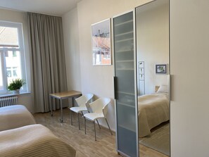 Una habitación de hotel moderna con una cama, un escritorio, dos sillas, una ventana con cortinas y un espejo.