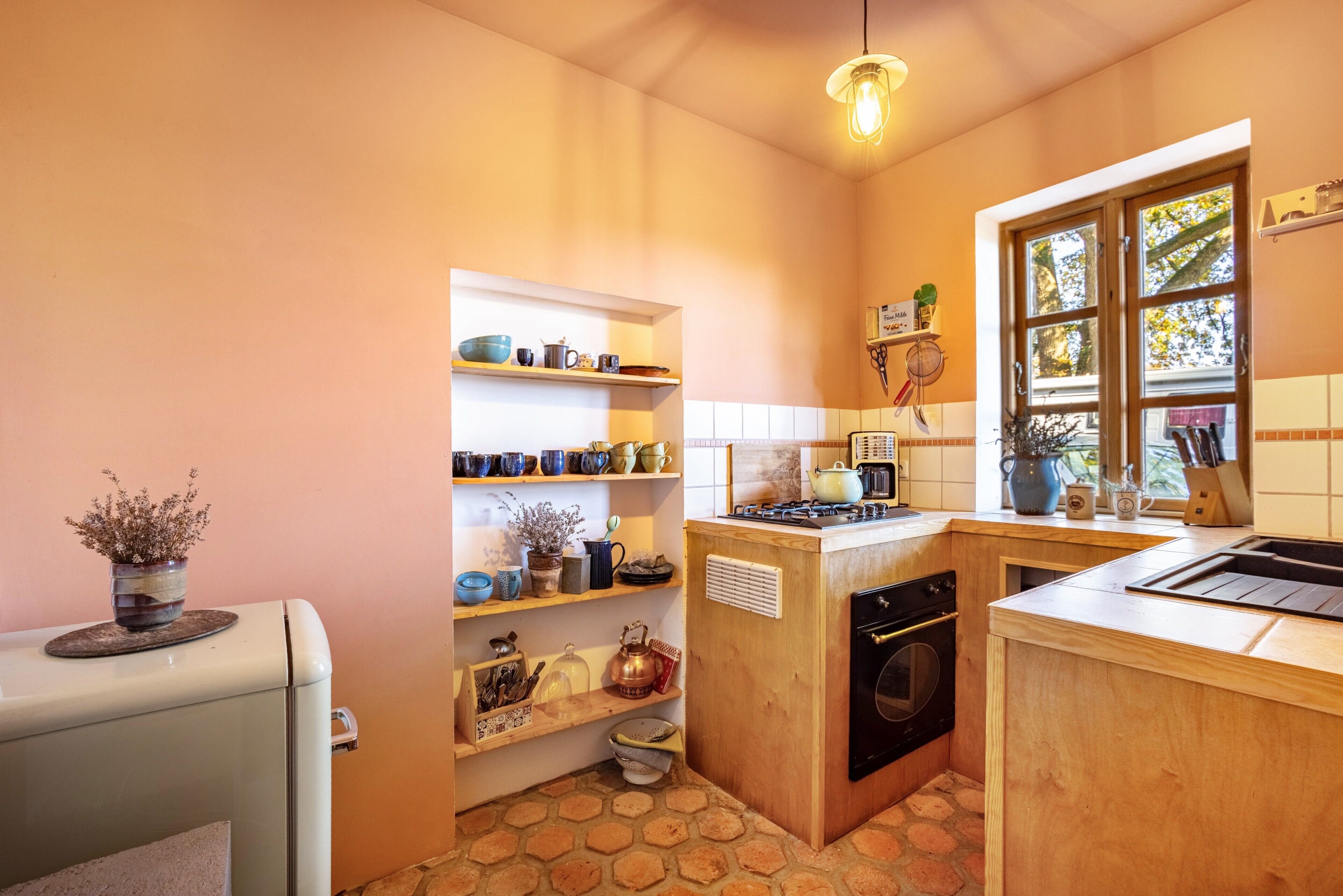 Une cuisine compacte avec des meubles en bois, une cuisinière encastrée et une fenêtre donnant sur la forêt.