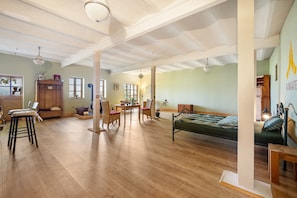 Una habitación amplia con suelo de madera, una cama, una mesa de comedor con sillas y un gran ventanal.