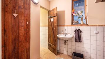Un baño con puerta de madera, un lavamanos blanco, un espejo con un florero y un perchero para toallas.