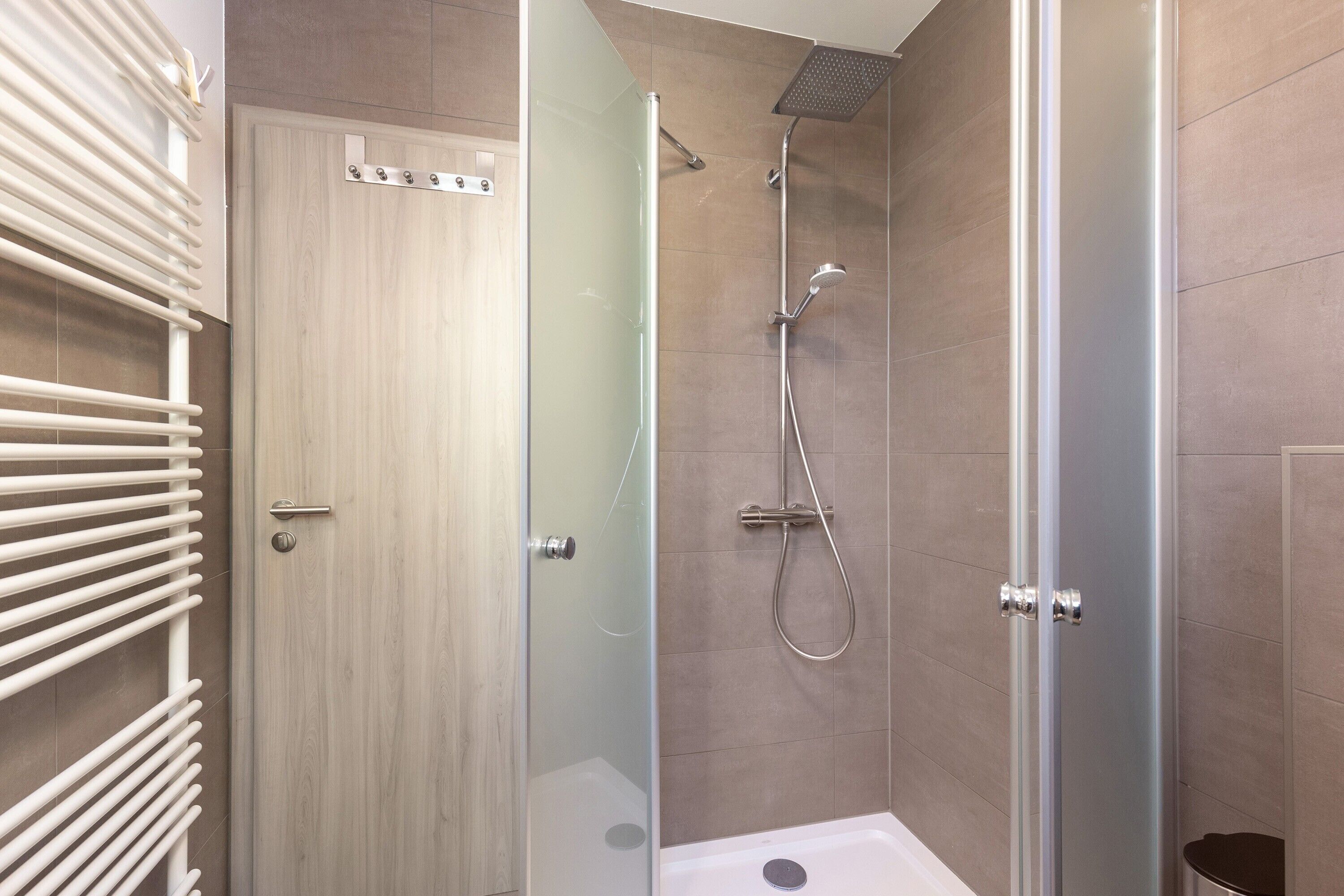 A modern shower enclosure with a glass door, a handheld showerhead, and a wall-mounted faucet.