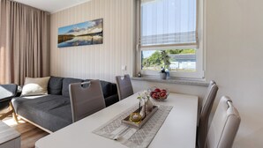 A modern living room with a sofa, dining table, and chairs. There is a window with curtains, a painting on the wall, and a vase with flowers on the table. - Apartment 'Ferienwohnung 2' with Shared Garden and Wi-Fi (Joachimsthal)