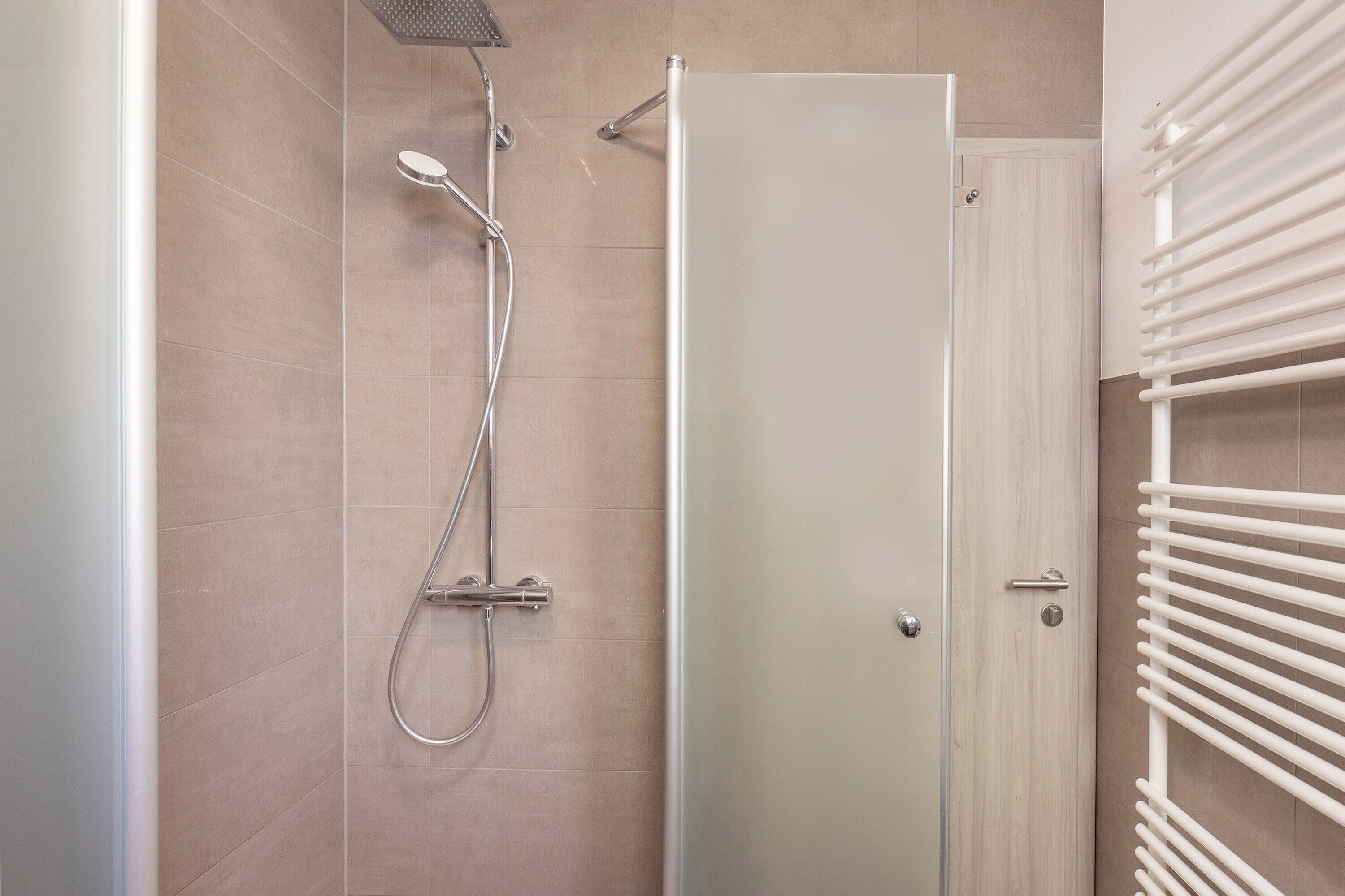 Un baño con ducha, una puerta y un perchero.