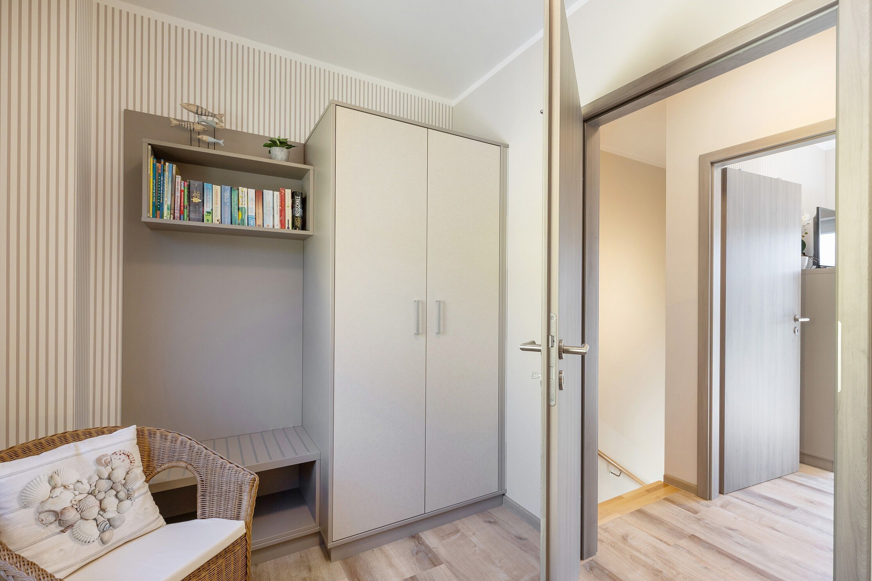 A room with a bookshelf, a wardrobe, a wicker chair, and a door leading to another room.