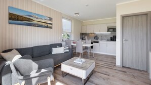 A modern living room with a grey sofa, a coffee table, and a dining area with a white table and chairs. A kitchen with white cabinets and appliances is visible in the background. - Apartment 'Ferienwohnung 2' with Shared Garden and Wi-Fi (Joachimsthal)