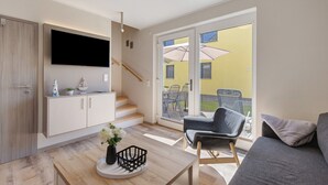 A modern living room with a flat-screen TV, a staircase, a dining area, and a view of the outside.