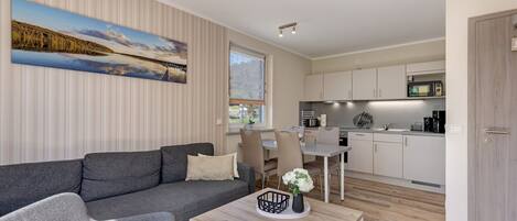 A modern living room with a grey sofa, a coffee table with a vase, and a dining area with chairs and a table.