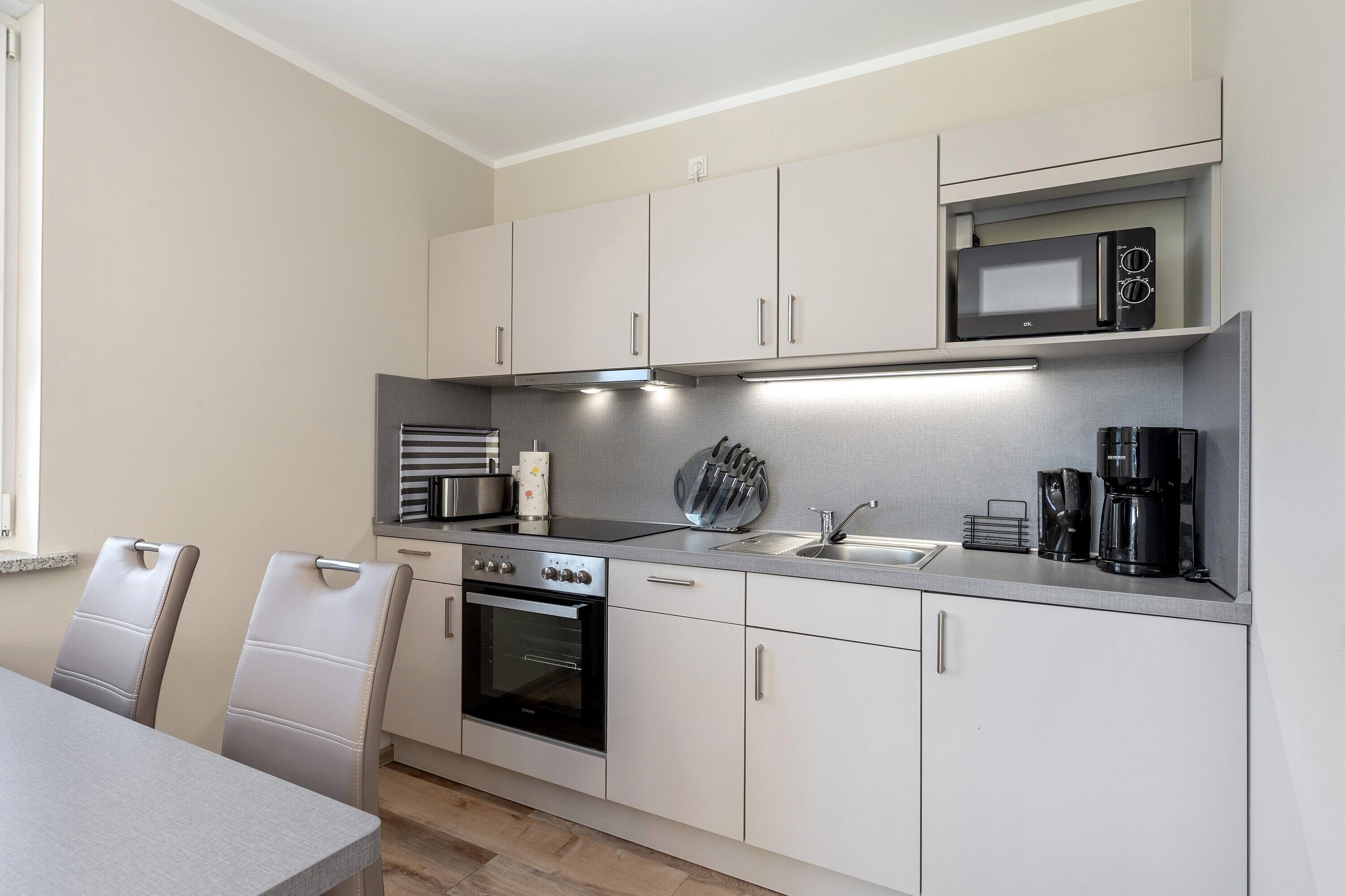 Een moderne keuken met witte kasten, een inbouwoven, een magnetron en een koffiezetapparaat.