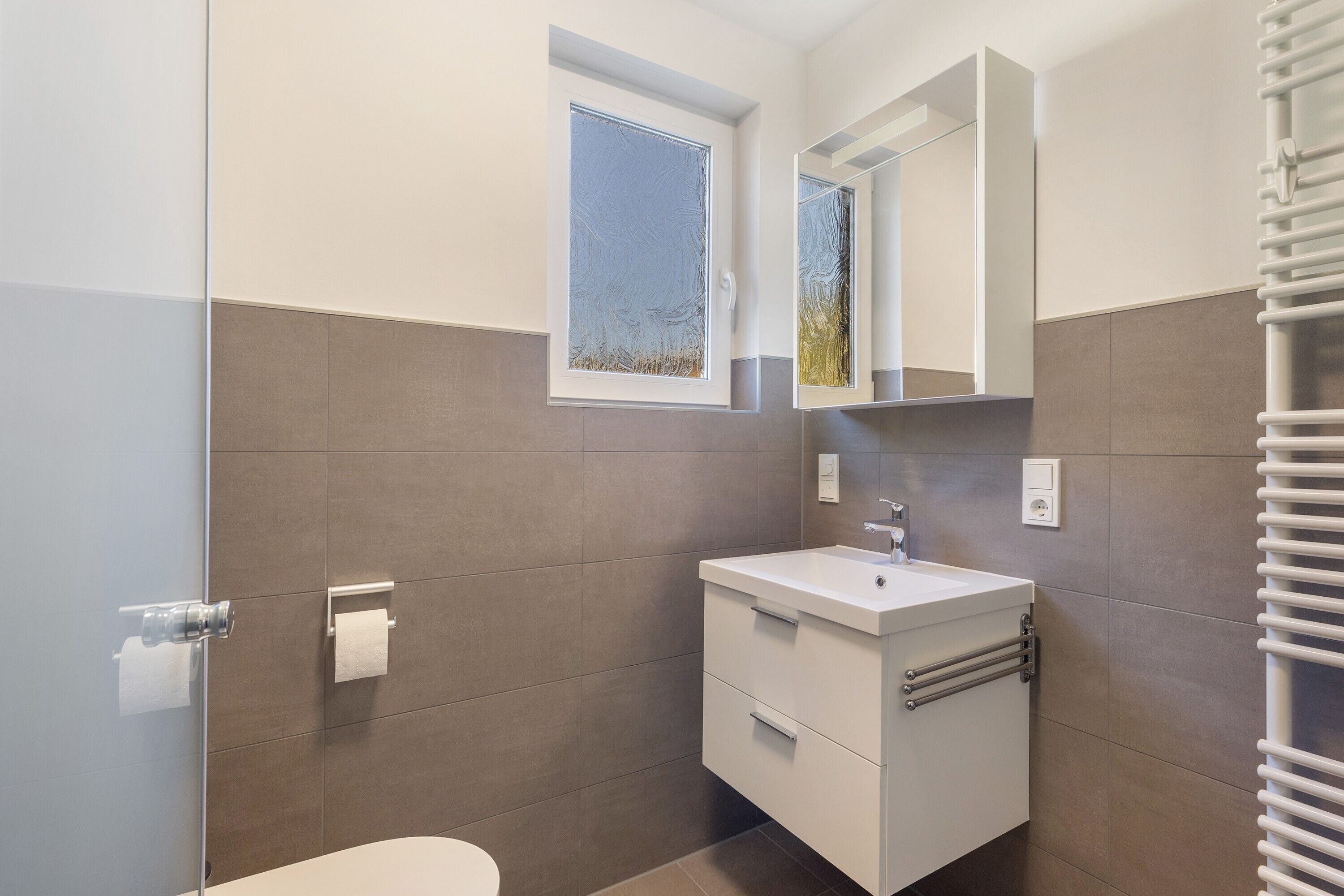 Ein modernes Badezimmer mit Toilette, Waschbecken mit Spiegel darüber und einem Handtuchhalter.