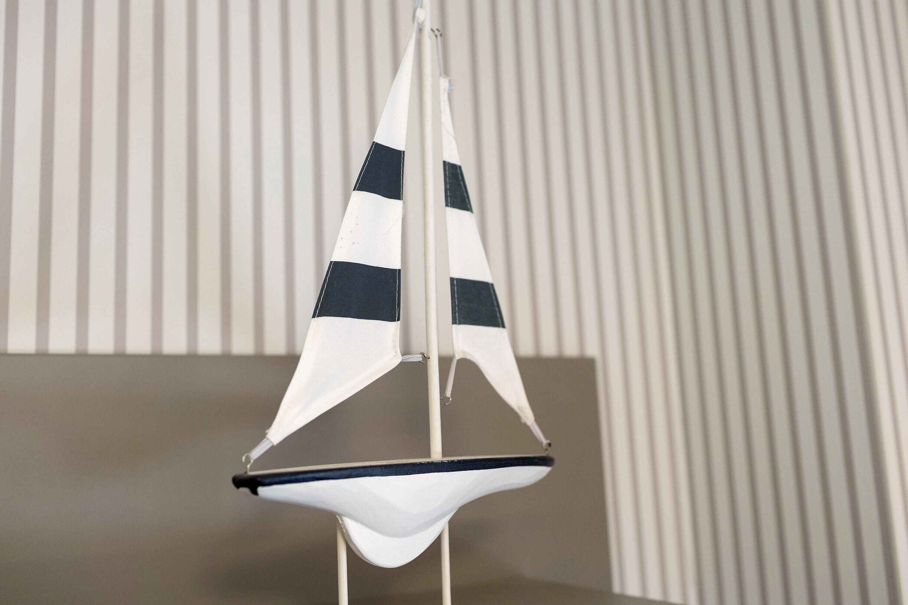 Un modellino di barca a vela con lo scafo bianco e vele blu scuro, sostenuto da un supporto bianco.