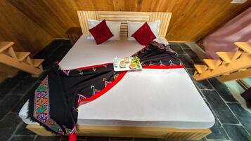 A bed with a white mattress, red pillows, and a black blanket with colorful embroidery. There is a tray with a cup and a small plate on the bed.