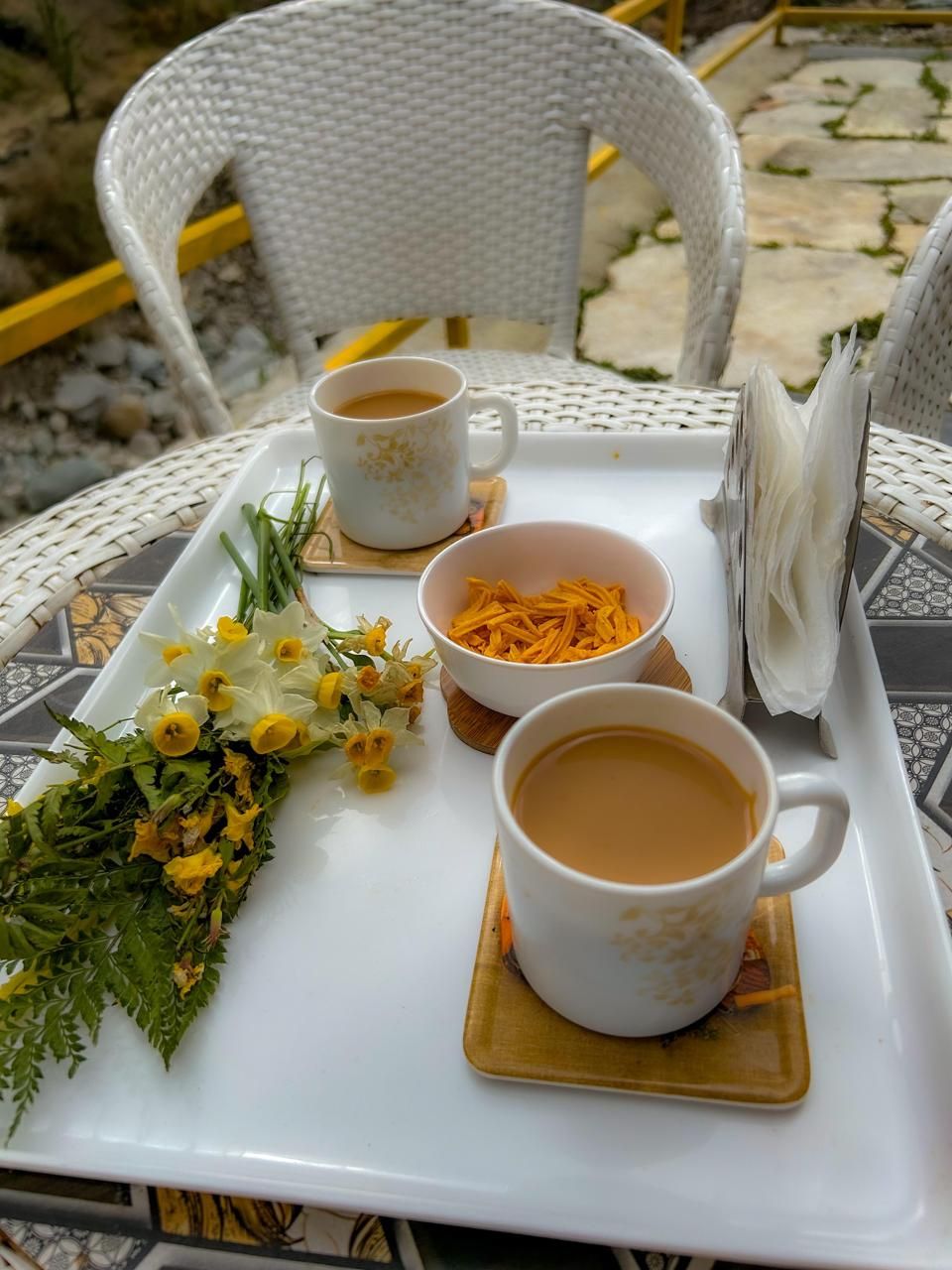 Une table avec deux tasses de café blanches, une assiette de carottes râpées, un petit bol de fleurs jaunes et un plateau avec un porte-serviettes.