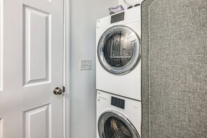 A laundry room with two stacked front-loading washing machines and a gray fabric barrier. - Home w/ Hot Tub, Playset & Grills in Clarksville! (Clarksville)
