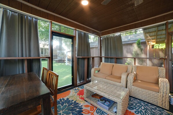A covered patio area with a wicker sofa, a wooden table, and a colorful rug. - Home w/ Hot Tub, Playset & Grills in Clarksville! (Clarksville)