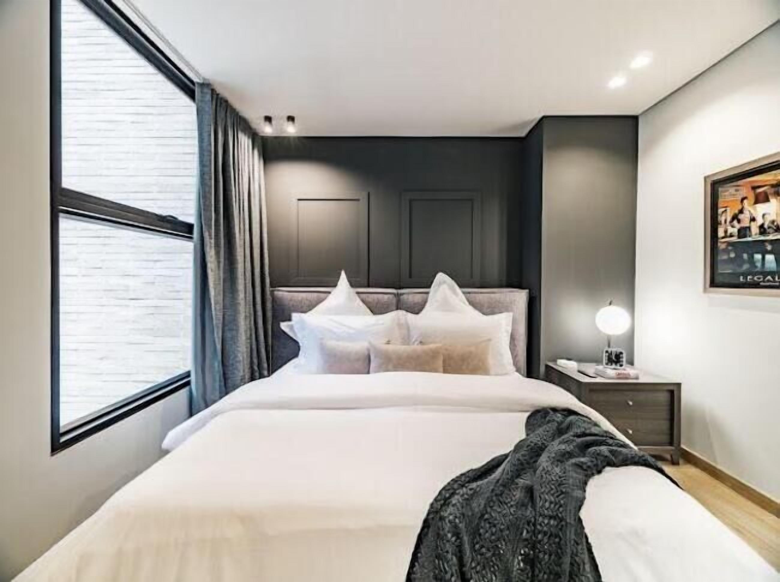 Ein modernes Hotelzimmer mit einem großen Bett, einem Nachttisch mit Lampe und einem Fenster mit Vorhängen.