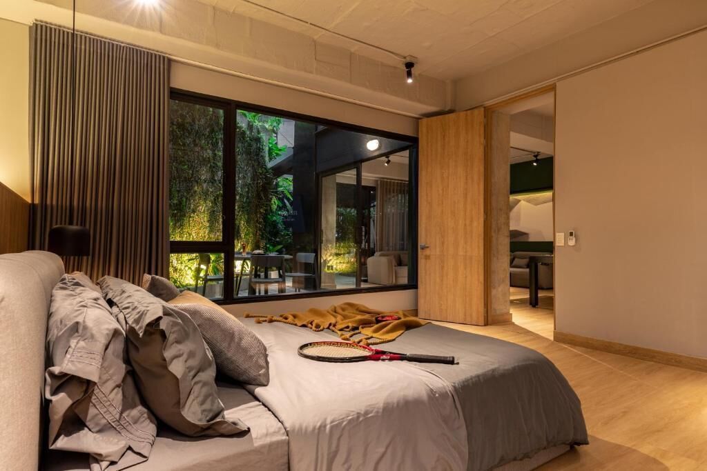 Un dormitorio moderno con un ventanal grande, una cama y vistas a un jardín exterior.