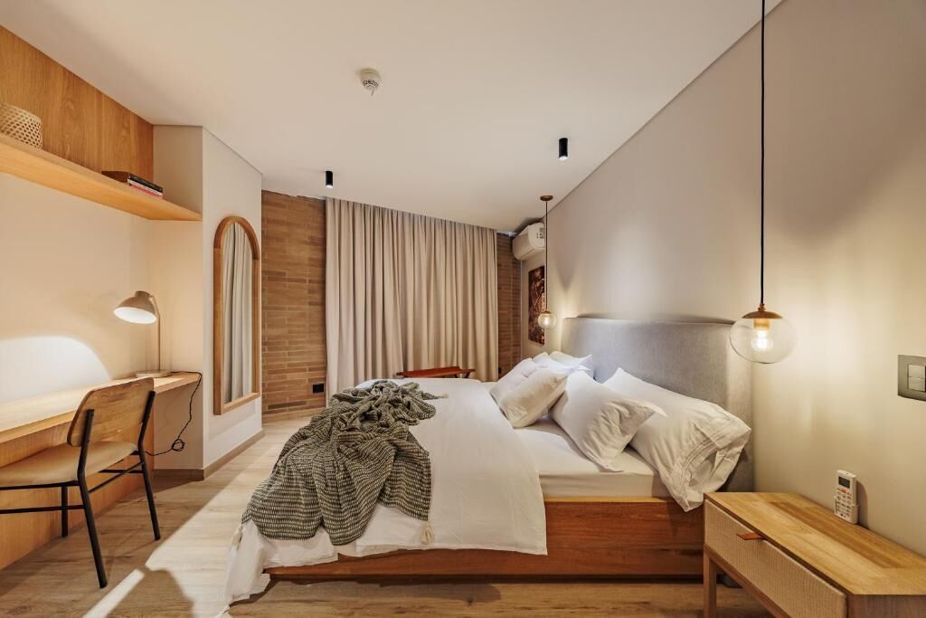 Una camera da letto moderna con una scrivania in legno, un letto con lenzuola bianche e una lampada a sospensione.