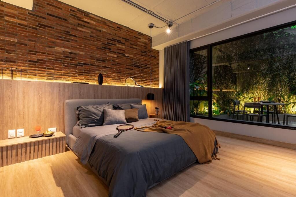 A modern bedroom with a large window, a wooden headboard, and a bedside table with a lamp.