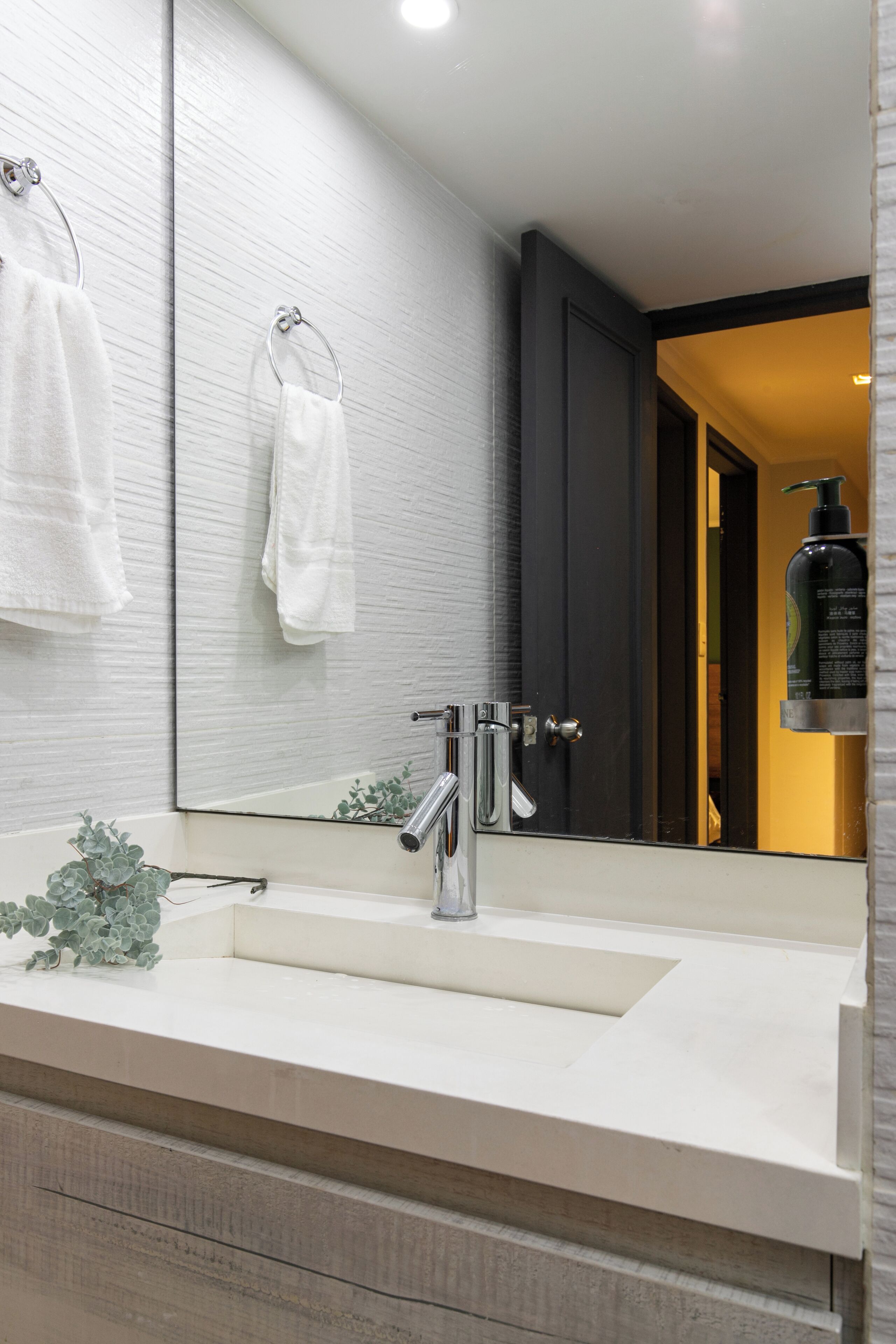 A modern bathroom with a large mirror, white sink, and two towel rings.