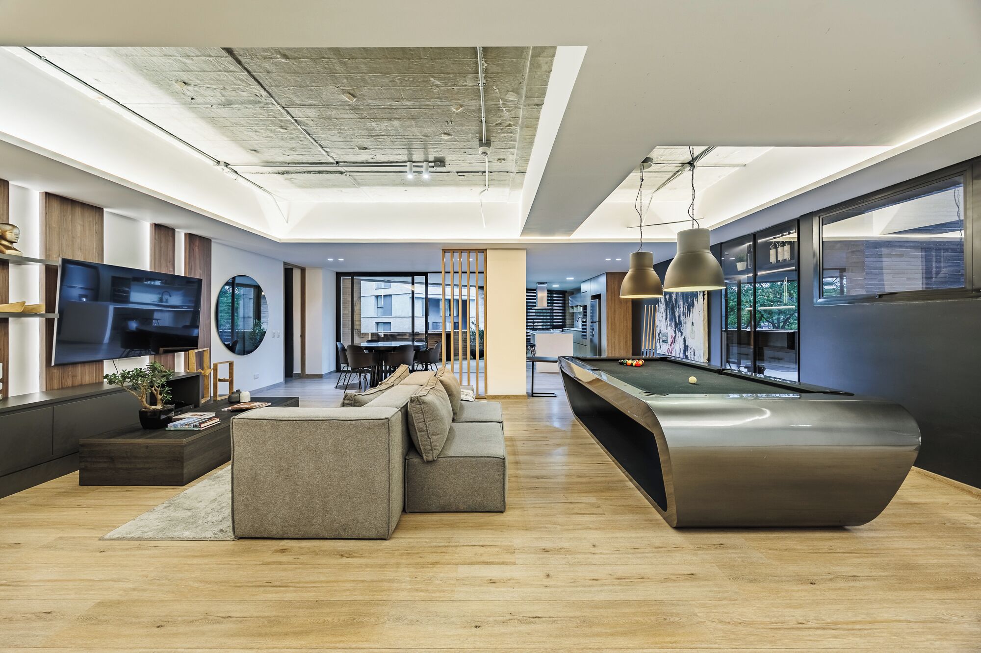 A modern living room with a pool table, comfortable seating, a flat-screen TV, and large windows offering views of the city.