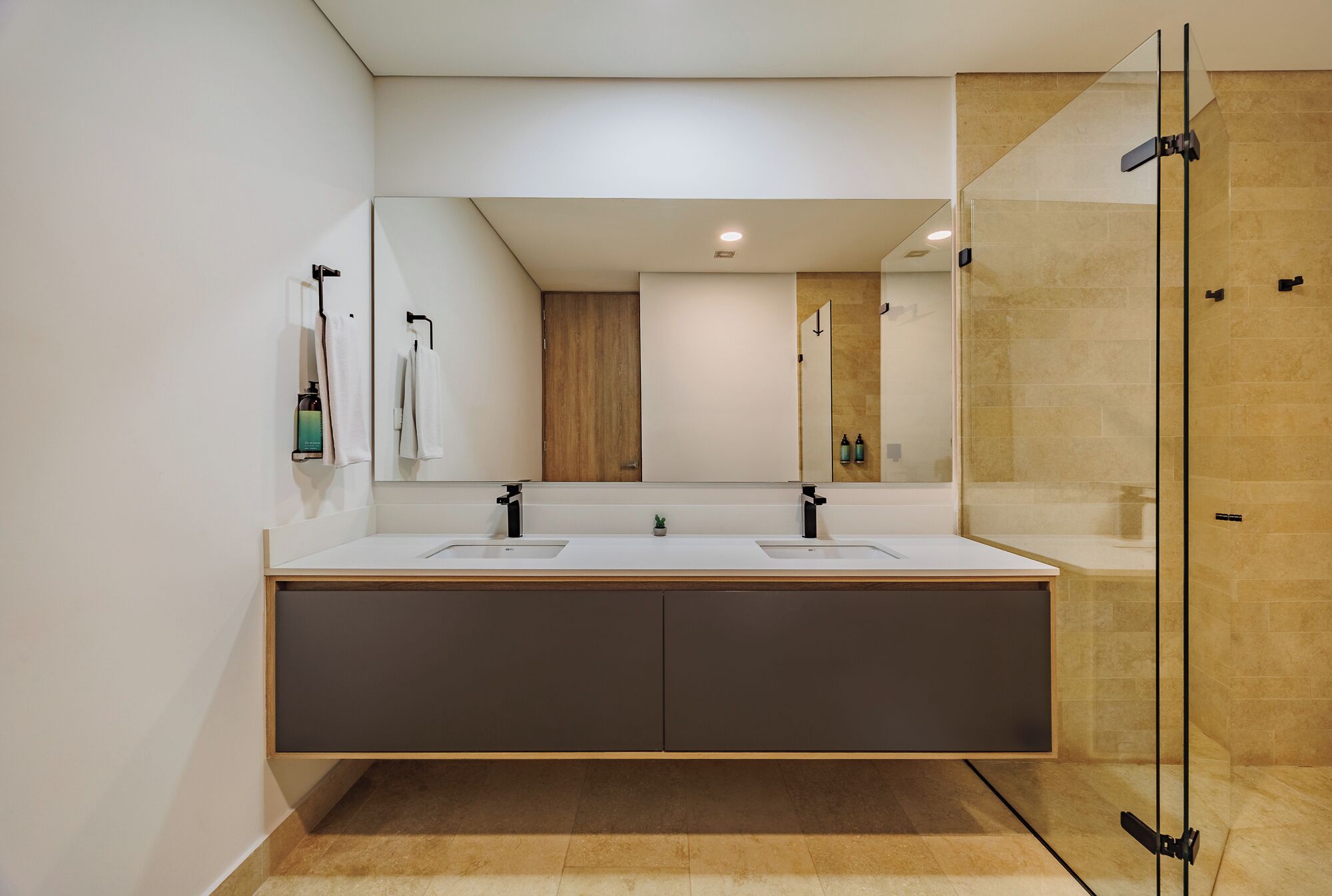 Een moderne badkamer met een grote spiegel, twee wastafels, een douchegedeelte en een houten kast.